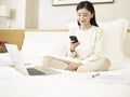 Young asian woman using cellphone and laptop on bed Royalty Free Stock Photo