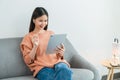 Young Asian woman using digital tablet and listen to relaxing music on the sofa at house.