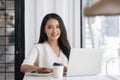 Young Asian woman using laptop in coffee shop and looking at camera. Royalty Free Stock Photo