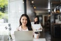 Young Asian woman using laptop in coffee shop and looking at camera. Royalty Free Stock Photo