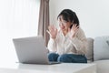 Young Asian woman using laptop computer for online video conference call waving hand making hello gesture on the couch in living Royalty Free Stock Photo