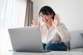 Young Asian woman using laptop computer for online video conference call waving hand making hello gesture on the couch in living Royalty Free Stock Photo