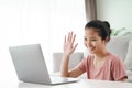 Young Asian woman using laptop computer for online video conference call waving hand making hello gesture in the living room Royalty Free Stock Photo