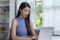 Young Asian woman using laptop at home, looking at screen, chatting, reading or writing email, sitting on desk Royalty Free Stock Photo