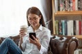 Young Asian woman using mobile phone and holding a hot cup of coffee, happy and relaxing time Royalty Free Stock Photo