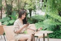 Young Asian woman using smart phone for chating or seaching information. A woman with smiley face in greeny garden
