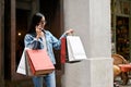 Young Asian woman using smartphone and carrying shopping bags while shopping at city mall Royalty Free Stock Photo