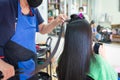 Young asian woman using smartphone while she getting a straight hair with hair straightener by hairdresser. Royalty Free Stock Photo