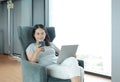 Young asian woman using smartphone and laptop computer working online at home and feel relaxing on armchair Royalty Free Stock Photo