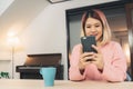 Young Asian woman using smartphone while lying on the desk in her living room. Happy female use phone for texting, reading, Royalty Free Stock Photo