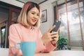 Young Asian woman using smartphone while lying on the desk in her living room. Happy female use phone for texting, reading, Royalty Free Stock Photo