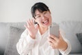 Young Asian woman using smartphone for online video conference call with friends waving hand making hello gesture Royalty Free Stock Photo