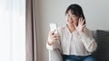 Young Asian woman using smartphone for online video conference call waving hand making hello gesture on the couch in living room Royalty Free Stock Photo