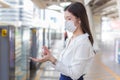 Young Asian woman is waiting for train at outdoors station while going to work at the office. She sprays alcohol to clean her hand