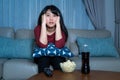 Young asian woman watching television suspense movie or news looking shocked and excited eating popcorn late night at home living