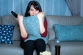 Young asian woman watching television suspense movie or news looking shocked and excited eating popcorn late night at home living