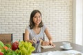 Young asian woman wear casual clothing holding pen with notebook on wooden table sitting in her kitchen. Work at home concept Royalty Free Stock Photo