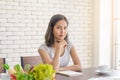 Young asian woman wear casual clothing holding pen with notebook on wooden table sitting in her kitchen. Work at home concept Royalty Free Stock Photo