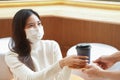 Young Asian woman wear face mask taking a cup of coffee from waiter at cafe Royalty Free Stock Photo