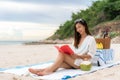 Young Asian woman wear sunglasses is relaxing with reading a book in the white sand beach and near sea with tropical fruit in Royalty Free Stock Photo