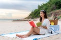 Young Asian woman wear sunglasses is relaxing with reading a book in the white sand beach and near sea with tropical fruit in Royalty Free Stock Photo