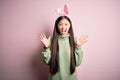 Young asian woman wearing cute easter bunny ears over pink background celebrating crazy and amazed for success with arms raised