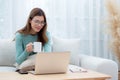 Young asian woman wearing glasses sitting sofa working on laptop computer and drinking coffee in living room. Royalty Free Stock Photo