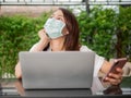 Young Asian woman wearing green medical mask looking up thinking while working with computer laptop and mobile phone at home Royalty Free Stock Photo