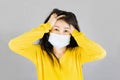 Young Asian woman wearing medical face mask and yellow shirt her hand on the head. isolated on gray background,health care concept