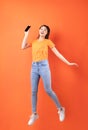 Young asian woman wearing orange T-shirt jumping on orange background Royalty Free Stock Photo