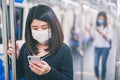 Young asian woman wearing protective face mask using smartphone in underground train due to the polluted air or pm 2.5 and