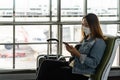 Young woman wearing sergical mask using smart phone while waiting for her flight at the airport Royalty Free Stock Photo