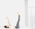 Beside of young asian woman wearing white undershirt and gray pants,exercising yoga while sitting on a white bed , stretch oneself Royalty Free Stock Photo