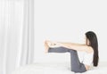 Beside of young asian woman wearing white undershirt and gray pants,exercising yoga while sitting on a white bed , stretch oneself Royalty Free Stock Photo