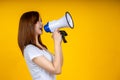 Young Asian woman in white casual t-shirt looking aside, scream in megaphone isolated on bright yellow Royalty Free Stock Photo