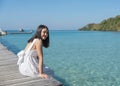 Young asian woman in white dress sitting on wooden pier in tropical sea on sunny day Royalty Free Stock Photo