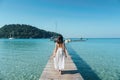 Young asian woman in white dress walking on wooden pier in tropical sea on sunny day Royalty Free Stock Photo