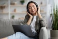 Young asian woman in wireless headphones enjoying music, using laptop Royalty Free Stock Photo