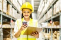 Young asian woman worker uses the phone for business contacts and holding clipboard to checking inventory in the warehouse