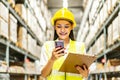 Young asian woman worker uses the phone for business contacts and holding clipboard to checking inventory in the warehouse