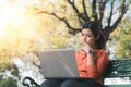 Young asian woman working with her laptop on and thinking about her online business bench in the park outdoors on vacation time Royalty Free Stock Photo