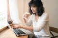 Young Asian woman working with laptop computer and drinking a cup of coffee. A woman with smiley face working from home. Social