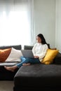 Young Asian woman working with laptop at home sitting on the couch in cozy apartment living room. Copy space. Royalty Free Stock Photo