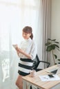 Young Asian woman writing notebook while standing behind working desk at home Royalty Free Stock Photo