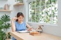 Young Asian woman writing in the notebook and using phone while sitting behind the window Royalty Free Stock Photo