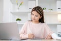 Young asian woman writting on digital tablet while looking at laptop computer, online learning, work from home