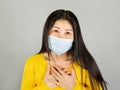 Young Asian woman in yellow shirt wearing medical face mask her hand on the chest isolated on gray background,health care concept Royalty Free Stock Photo