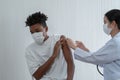 Young Asian woman doctor wear mask is giving injections or vaccines to arm of African American boy who fear syringe at hospital Royalty Free Stock Photo