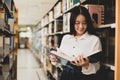 Young Asian women are searching for books and reading from the bookshelves in the college library to research and develop Royalty Free Stock Photo