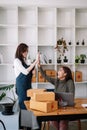 Young asian women teamwork partners packing order into box together using touchpad to do delivery to client. two female